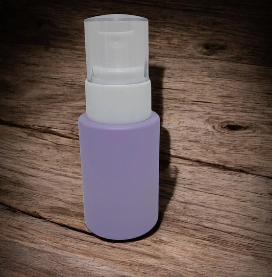Frosted lavender glass cosmetic pump bottle with white dispenser on wood surface