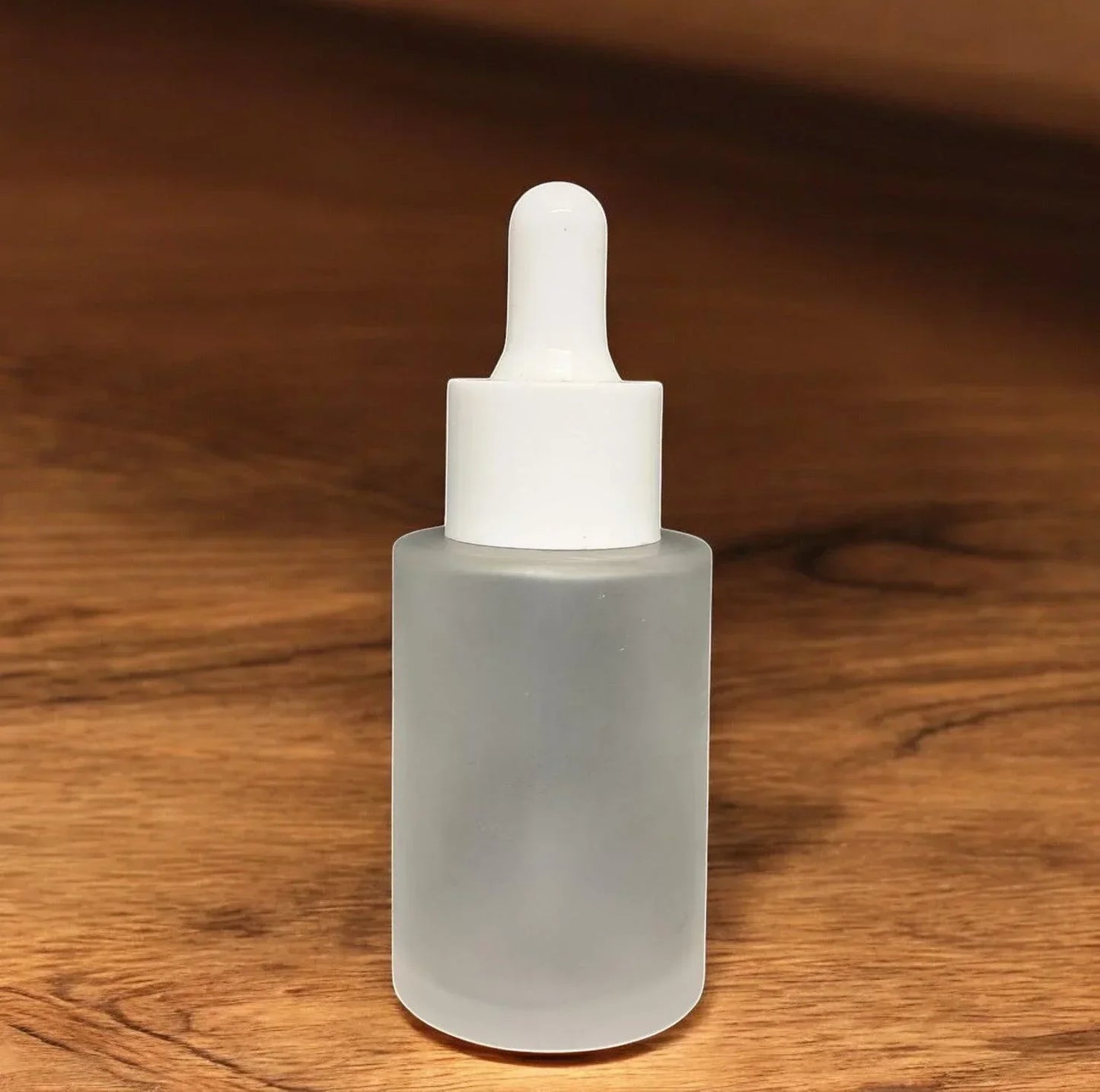 Frosted glass dropper bottle with white cap on wooden surface, cosmetic packaging
