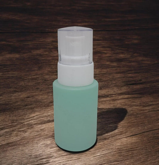Frosted green glass cosmetic pump bottle with white cap on wooden surface