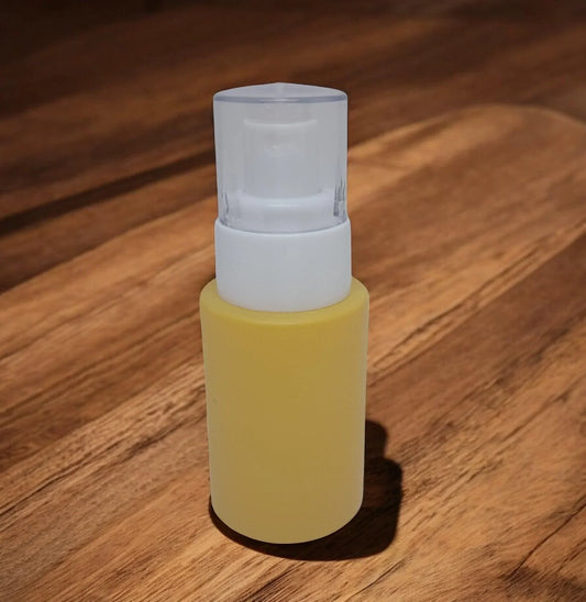 Frosted glass cosmetic pump bottle with yellow liquid and white cap on wooden surface