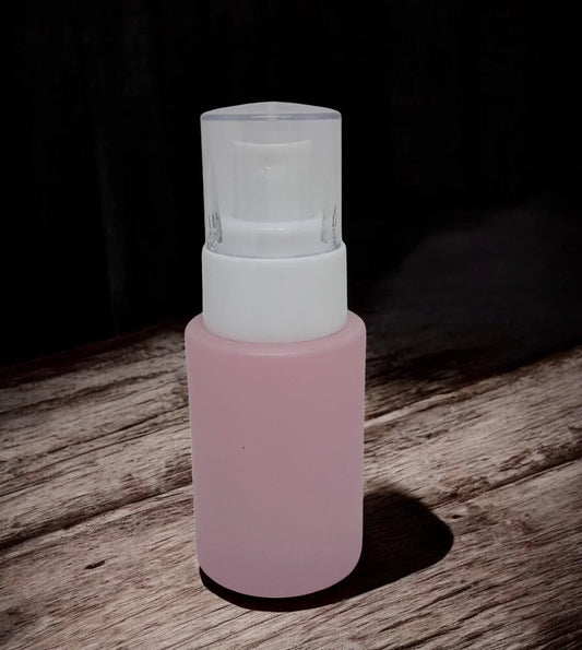 Pink frosted glass cosmetic pump bottle with white dispenser on wooden surface